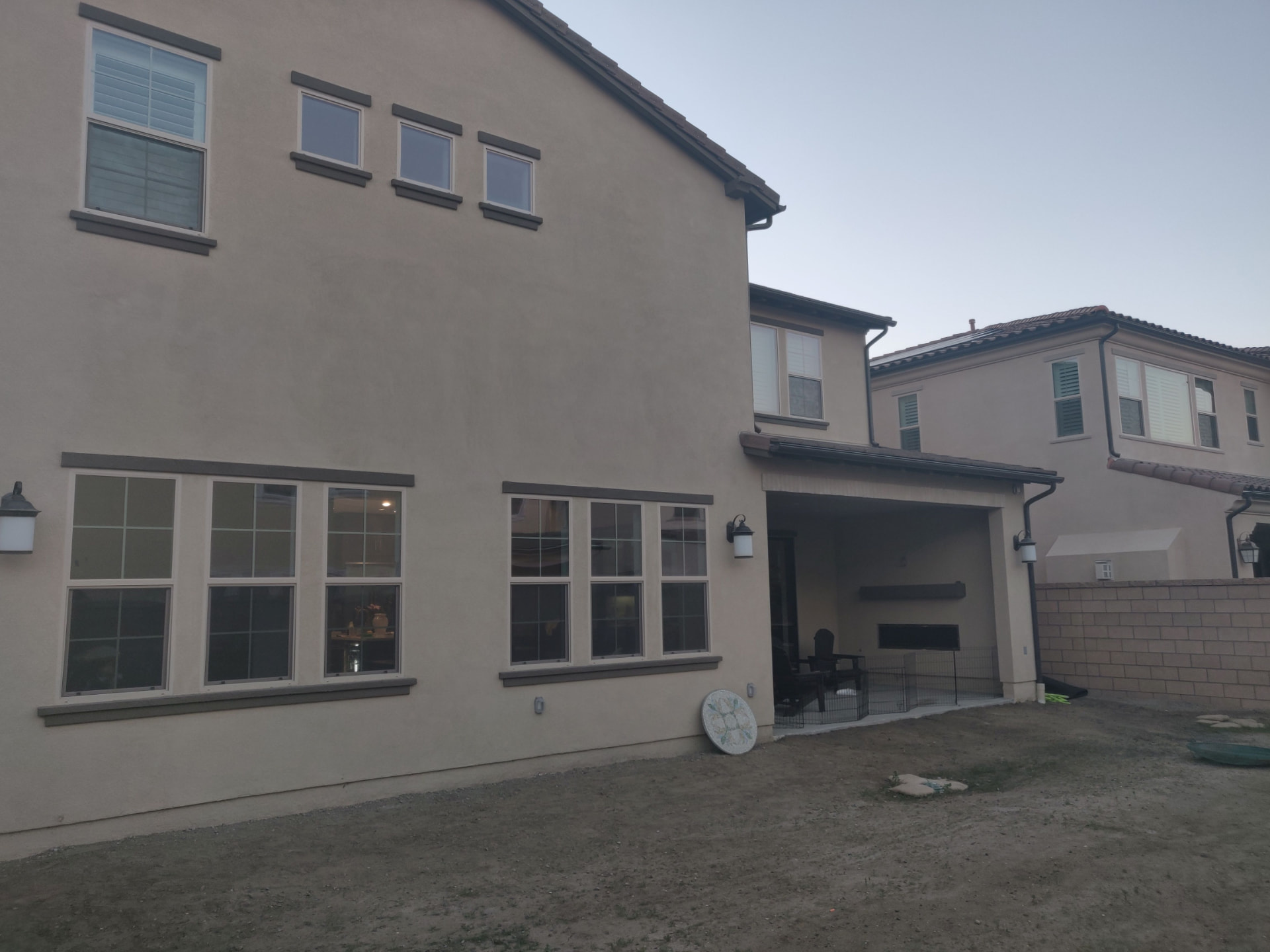 Existing condition photograph of a new tract home backyard in Huntington Beach with graded dirt, block walls, and an empty covered California Room.